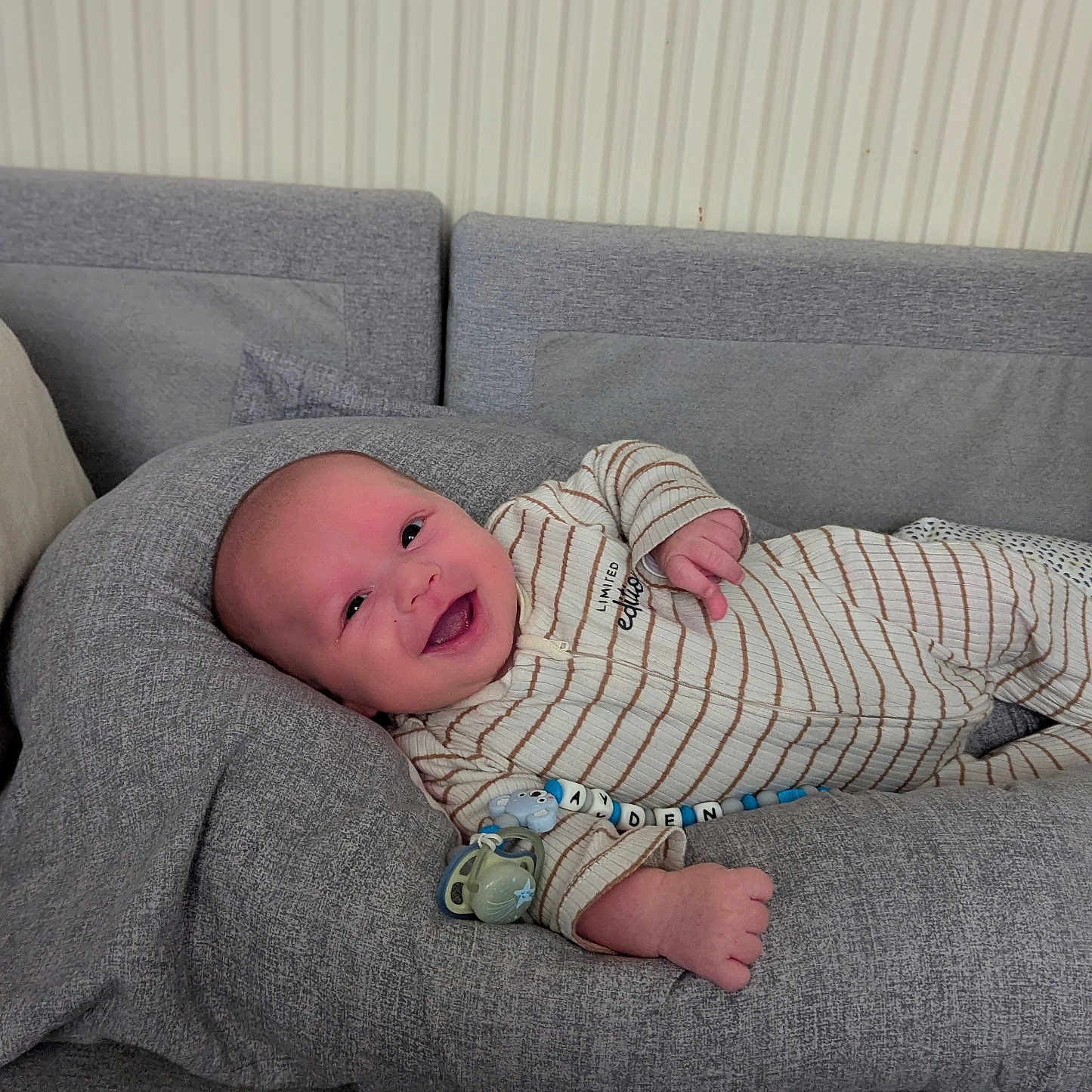 Ayden a rejoint le concours — aidez-le/la à gagner de superbes lots ! baby, child, comfort, cozy, cushion, cute, gray, happy, home, indoor, infant, onesie, pacifier, person, portrait, relaxing, seat, smiling, striped, young