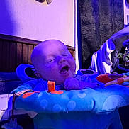 Malachi joined the competition — help win amazing prizes! baby, infant, child, yawning, mouth_open, purple_lighting, toy, activity_center, bouncer, indoor, portrait, face, head, plush_toy, fabric, curtain, wood_paneling, pacifier, strap, seat