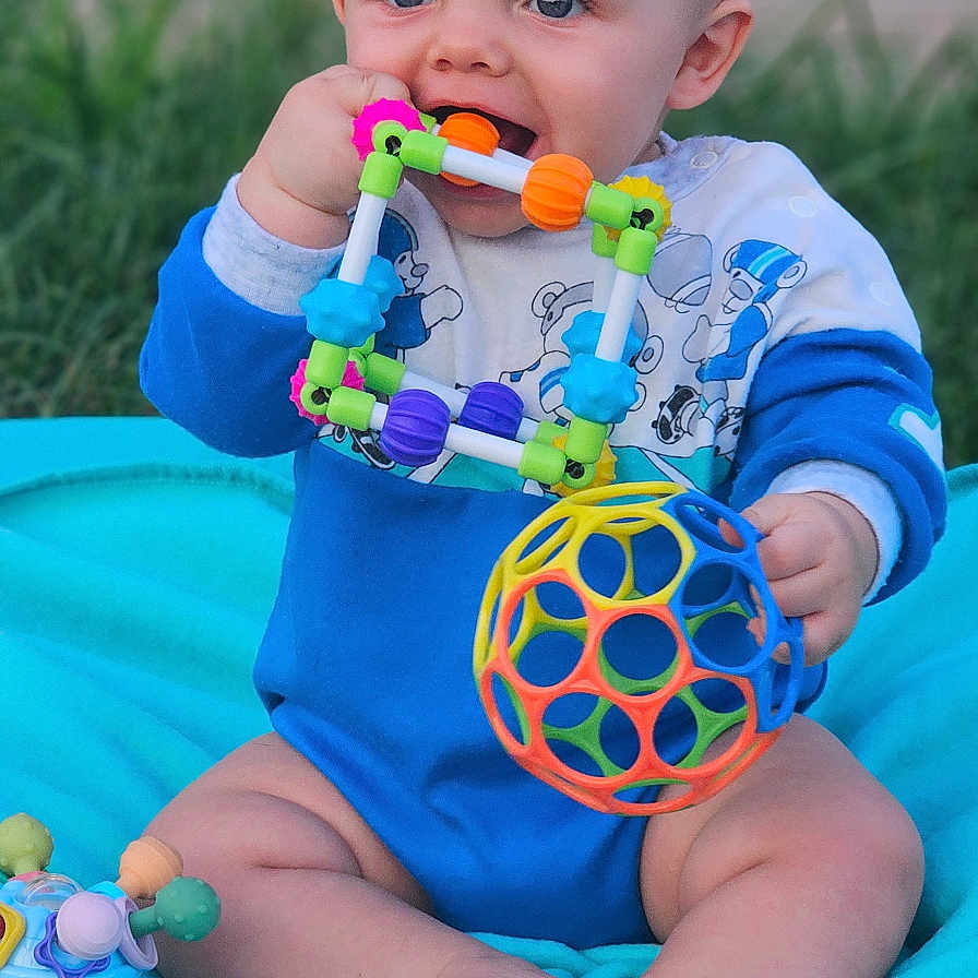 Liam joined the competition — help win amazing prizes! baby, blanket, bodypart, clothing, cutlery, face, finger, food, grass, hand, head, person, photography, plant, portrait, rattle, sitting, sweets, t_shirt, toy
