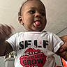 Aayan joined the competition — help win amazing prizes! baby, black_hair, candid, casual_clothing, child, cute, earrings, fireplace, graphic_tshirt, hand, home, indoor, living_room, person, playful, portrait, smiling, toddler, tongue_out, white_shirt