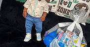 Aayan joined the competition — help win amazing prizes! blue, child, couch, decor, face, football, gift_basket, indoor, pacifier, pants, person, pillow, plastic_wrap, ribbon, shirt, sneakers, standing, toddler, toy, white