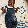 baby, infant, denim_overalls, striped_shirt, milestone_blanket, numbers, blue_circle, smiling, face, hands, feet, cute, child, lying_down, cozy, patterned_blanket, dinosaur_patch, months_marker, age, portrait