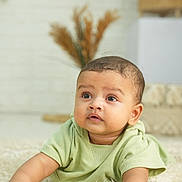 Darvik is registered to the contest to win money with this photo: baby, infant, child, green_clothing, lying_down, carpet, rug, indoor, portrait, cute, curious, soft_lighting, cozy, decor, neutral_colors, face, skin, hand, expression, young