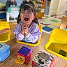 child, toddler, happy, smiling, indoor, classroom, colorful, toy, soft_toy, table, wooden_table, yellow_chair, person, face, play, cute, young_child, clothing, hair, furniture