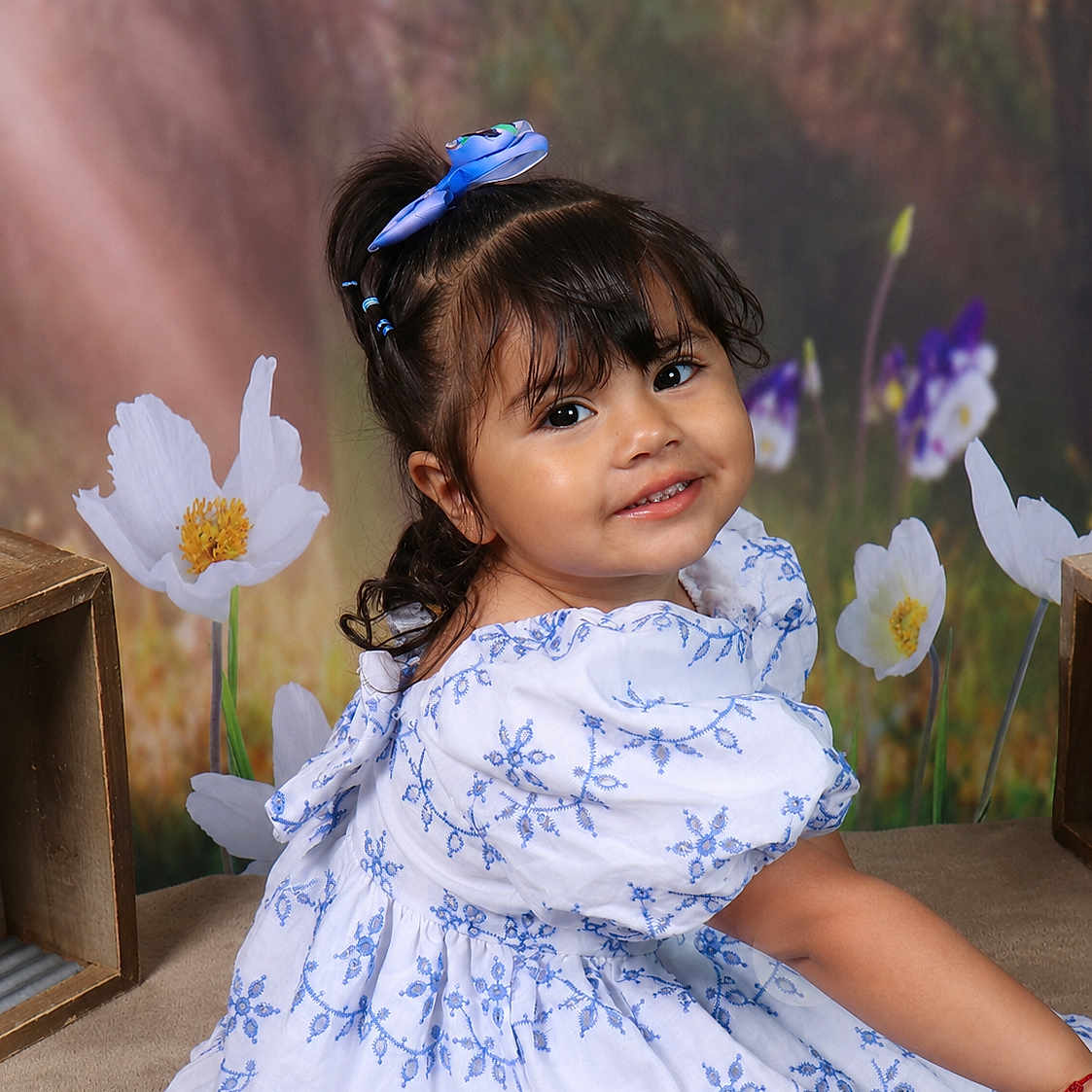 Arabella is registered to the contest to win money with this photo: child, girl, smile, dress, blue_bow, flowers, portrait, cute, happy, curly_hair, embroidery, sitting, studio, background, flower_pattern, young, pretty, innocent, posing, colorful