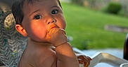 Santiago joined the competition — help win amazing prizes! baby, child, high_chair, macaroni_and_cheese, food, messy, hand, face, cheeks, curious, outdoor, greenery, sunlight, table, feeding, meal, infant, cute, portrait, sitting