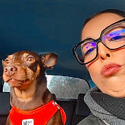 Mozart a rejoint le concours — aidez-le/la à gagner de superbes lots ! dog, person, glasses, scarf, car, orange_harness, brown_dog, seat, window, daylight, portrait, face, closeup, travel, vehicle_interior, casual_clothing, happy, alert, side_by_side, winter