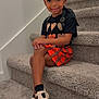 child, girl, smiling, stairs, carpet, black_shirt, orange_skirt, plaid_skirt, shoes, bows, curly_hair, earrings, pose, indoor, wall, happy, fashion, portrait, person, cute