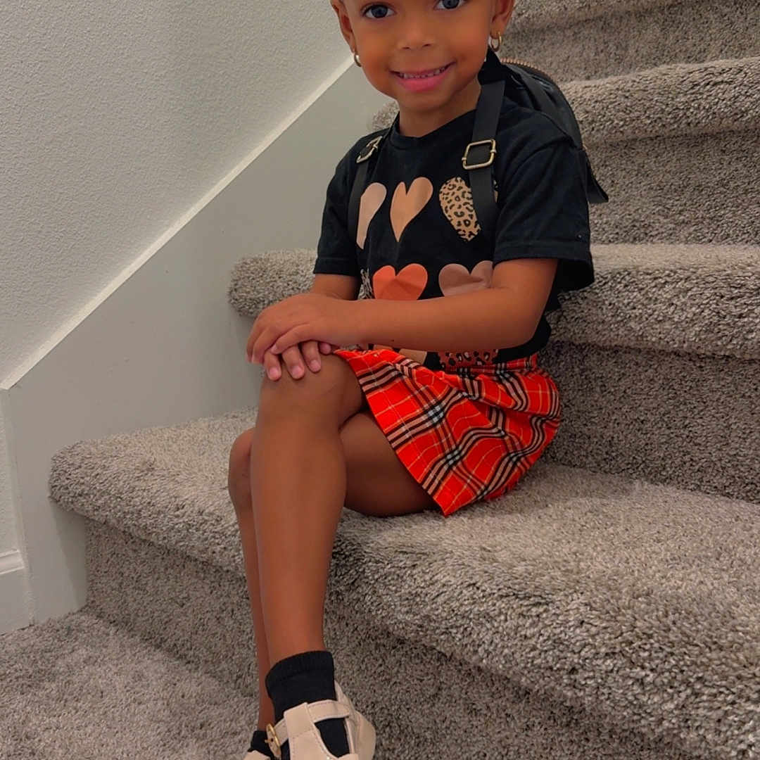 Jaiya is registered to the contest to win money with this photo: black_shirt, bows, carpet, child, curly_hair, cute, earrings, fashion, girl, happy, indoor, orange_skirt, person, plaid_skirt, portrait, pose, shoes, smiling, stairs, wall