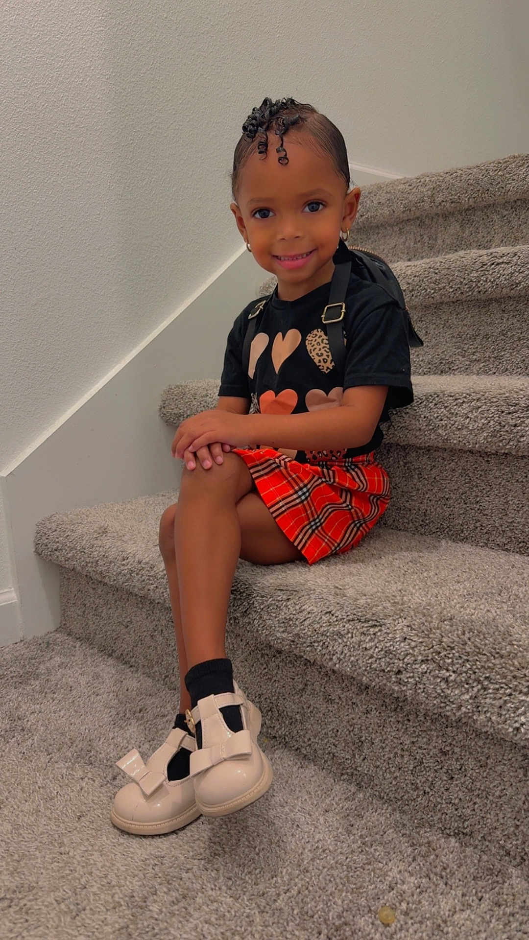 Jaiya is registered to the contest to win money with this photo: child, girl, smiling, stairs, carpet, black_shirt, orange_skirt, plaid_skirt, shoes, bows, curly_hair, earrings, pose, indoor, wall, happy, fashion, portrait, person, cute