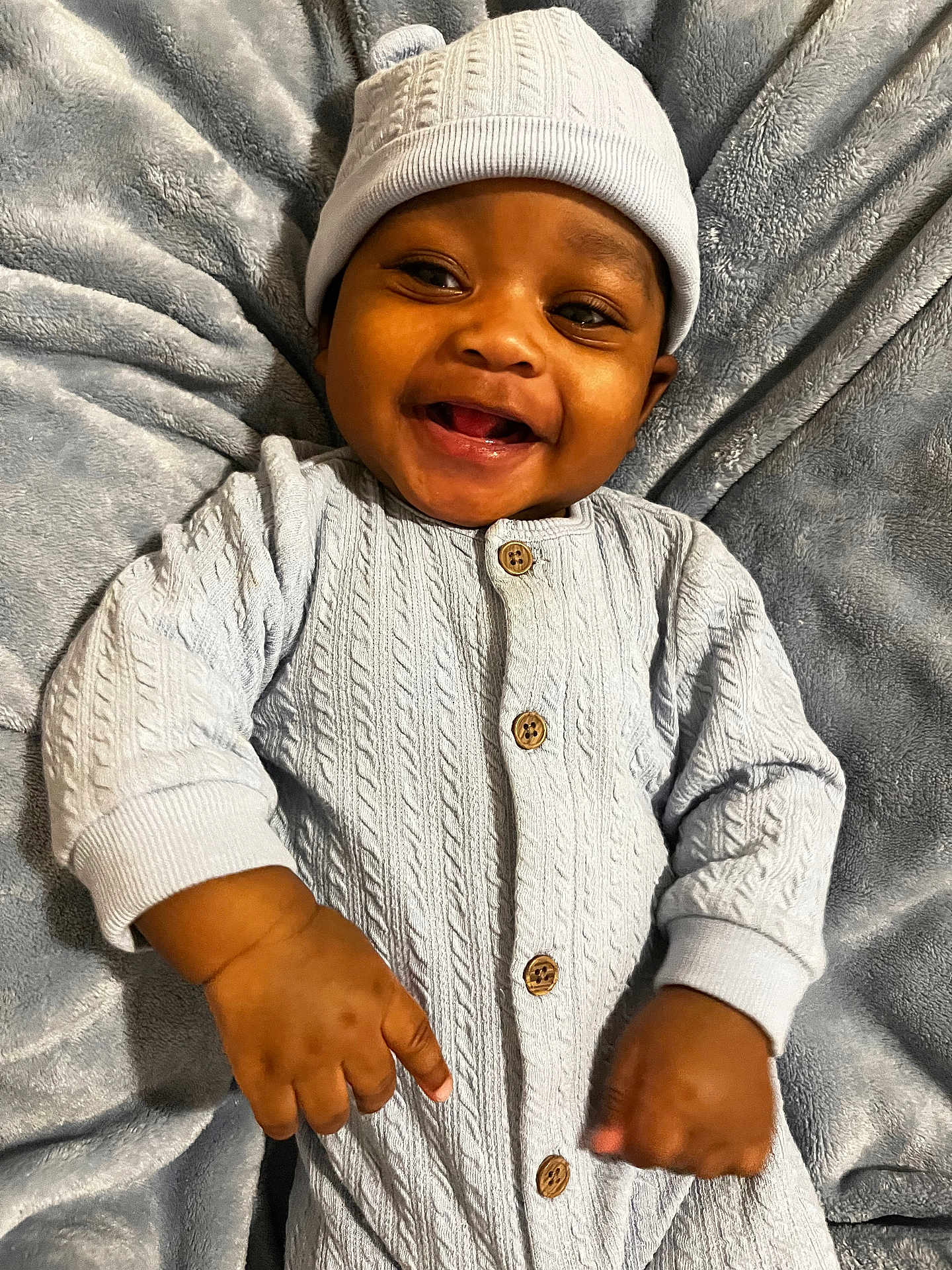 Kenai joined the competition — help win amazing prizes! baby, smiling, infant, blue_hat, knitted_outfit, blanket, soft_texture, happy, cute, child, portrait, indoors, warm_clothing, hands, face, buttoned_outfit, lying_down, cozy, newborn, expressive