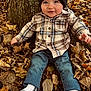 autumn_leaves, baby, beanie, blue_eyes, casual_clothing, child, cute, fall, hat, jeans, nature, outdoors, person, plaid_shirt, portrait, sitting, smiling, socks, toddler, tree_trunk