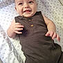 baby, smiling, infant, star_pattern, mattress, brown_outfit, sleeveless, cute, child, happy, lying_down, indoor, person, skin, hand, face, head, eyes, mouth, fingers