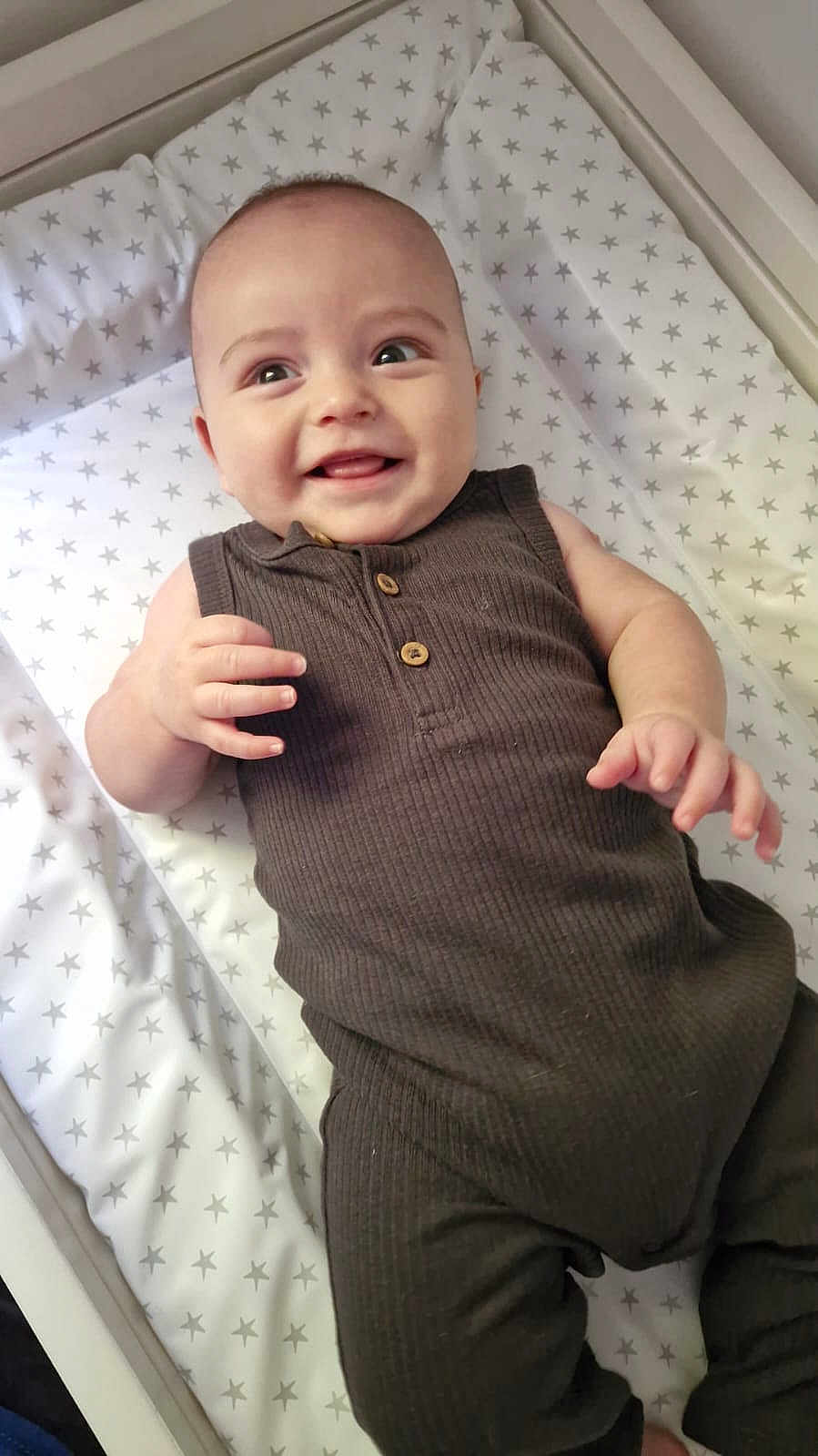 Max joined the competition — help win amazing prizes! baby, smiling, infant, star_pattern, mattress, brown_outfit, sleeveless, cute, child, happy, lying_down, indoor, person, skin, hand, face, head, eyes, mouth, fingers