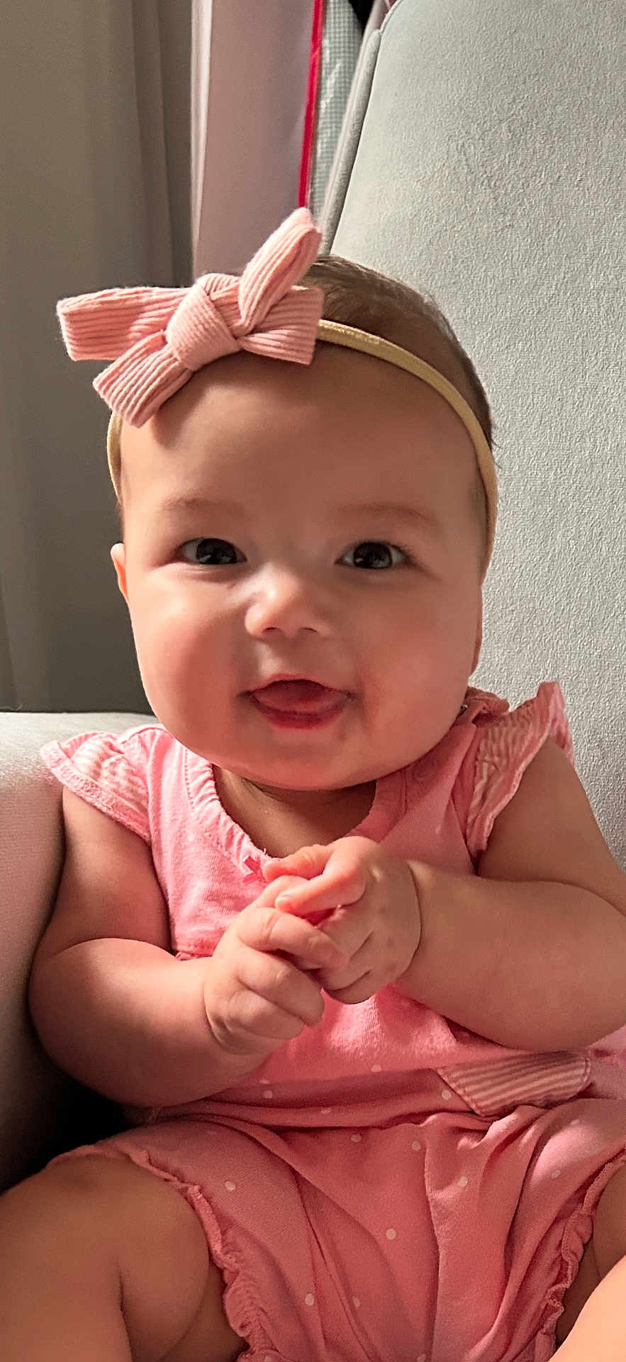 Gianna is registered to the contest to win money with this photo: baby, child, pink_outfit, headband, bow, smiling, tongue_out, hands_clasped, sitting, indoor, chair, cute, happy, infant, portrait, chubby_cheeks, natural_light, clothing, person, young_child