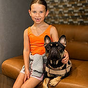 Bosa joined the competition — help win amazing prizes! animal, brown, casual_clothing, child, companion, couch, dog, french_bulldog, friendly, girl, happy, indoor, leather_furniture, orange_tank_top, pet, portrait, shorts, sitting, smile, young