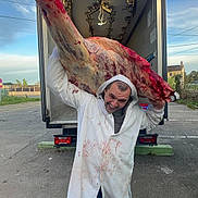 Itah participe au concours pour gagner de l'argent avec cette photo : man, white_coat, blood_stains, carcass, meat, truck, open_truck, outdoor, sky, pavement, industrial, delivery, workwear, smiling, person, meat_processing, butcher, transport, daytime, rural