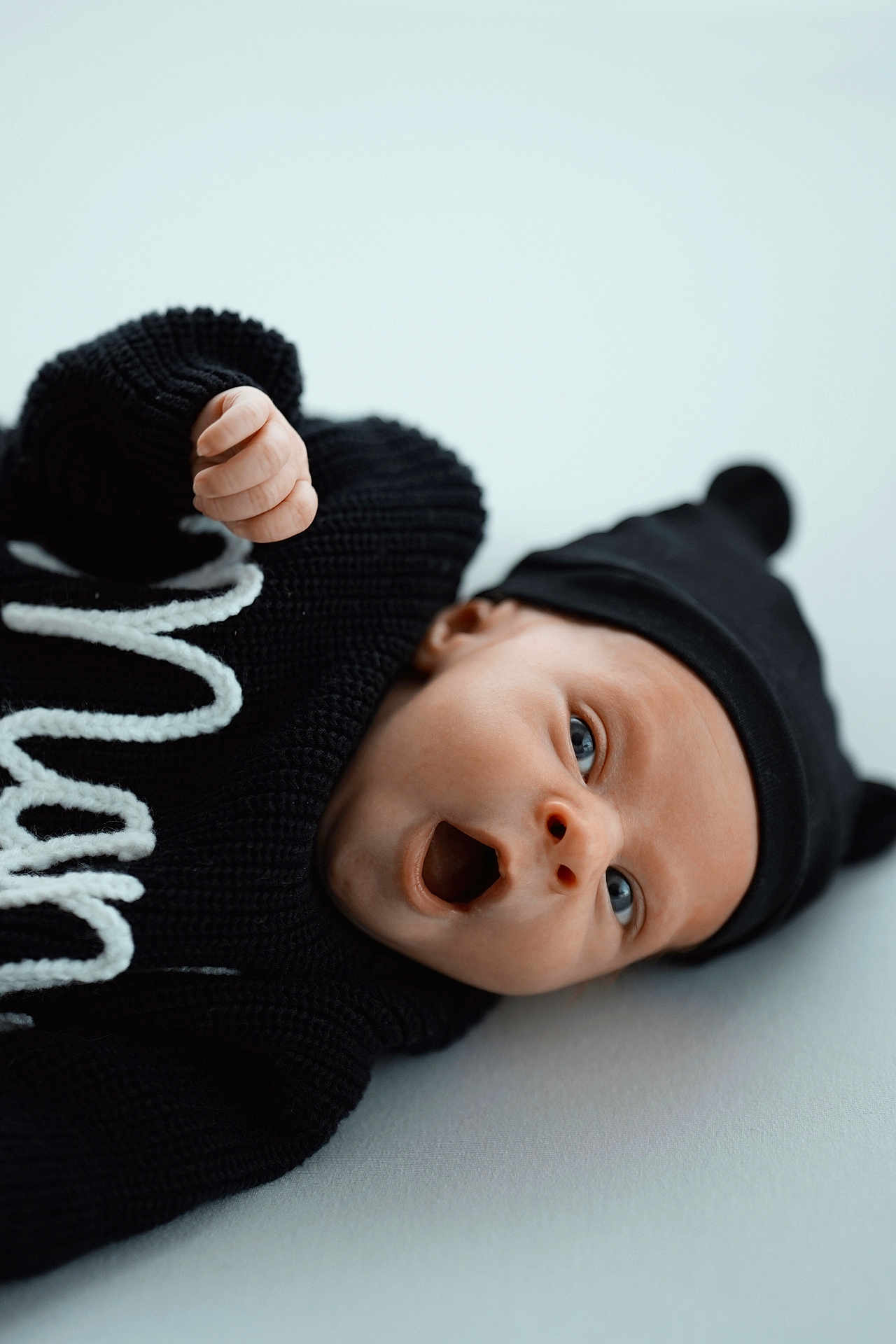 Manel a rejoint le concours — aidez-le/la à gagner de superbes lots ! baby, infant, blue_eyes, black_hat, black_sweater, knitwear, cute, lying_down, expression, mouth_open, soft_surface, portrait, child, newborn, hat_with_ears, closeup, indoor, warm_clothing, face, person