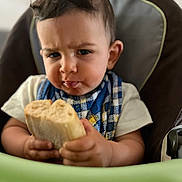 Lyham participe au concours pour gagner de l'argent avec cette photo : toddler, child, bread, food, high_chair, expression, serious, face, hands, clothing, bib, indoor, portrait, baby, person, eating, snack, seat, home, cute