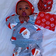 Edwin is registered to the contest to win money with this photo: baby, infant, child, christmas, santa_pajamas, red_hat, tinsel_tree, gift_box, surprised_expression, lying_down, blanket, bed, holiday, festive, cozy, portrait, cute, wide_eyes, mouth_open, indoor
