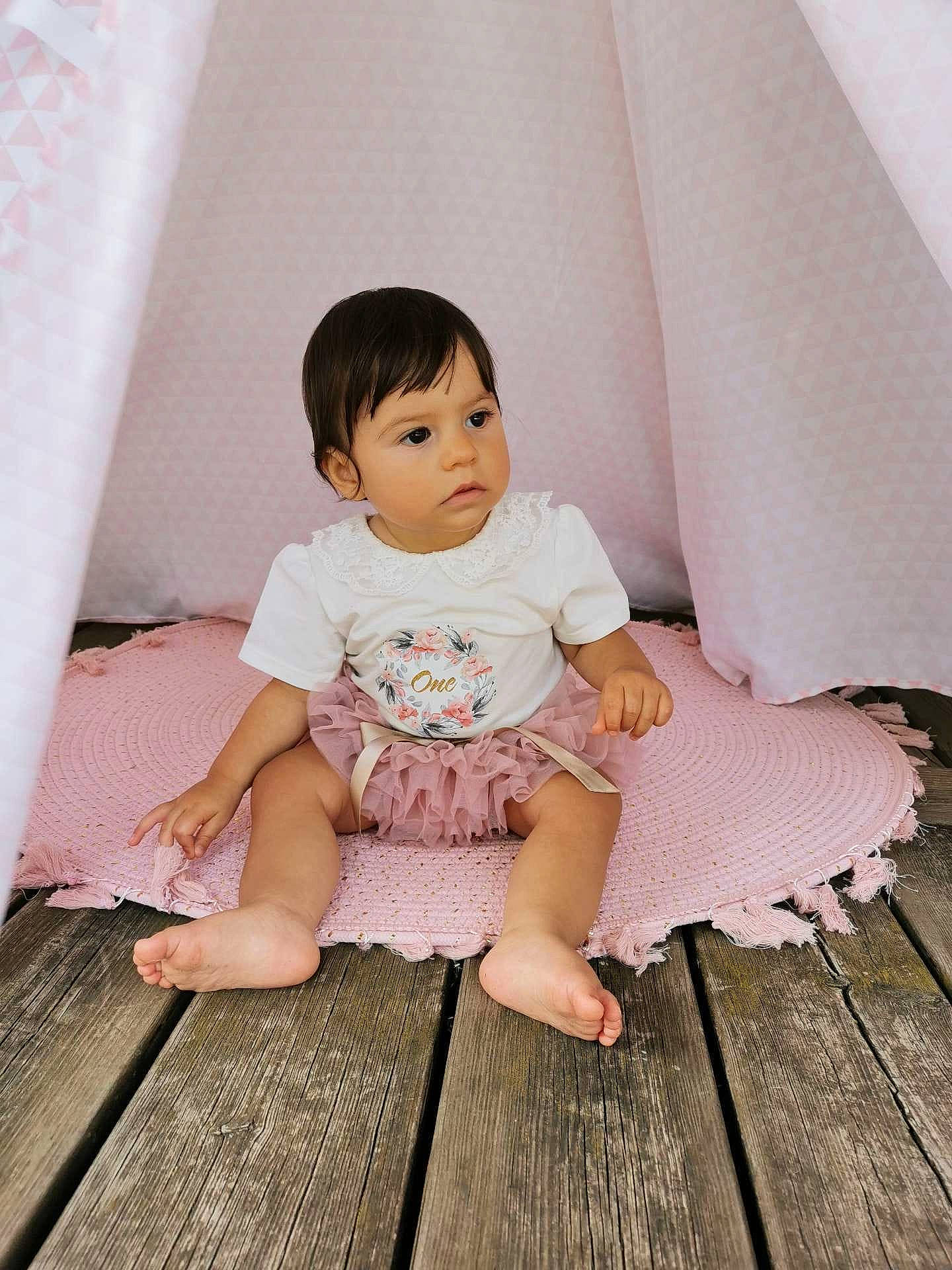 Anastazia participe au concours pour gagner de l'argent avec cette photo : baby, baby_toddler_clothing, child, comfort, dress, facial_expression, finger, floor, flooring, foot, grass, hardwood, human_leg, joint, person, pink, skin, sleeve, thigh, toddler