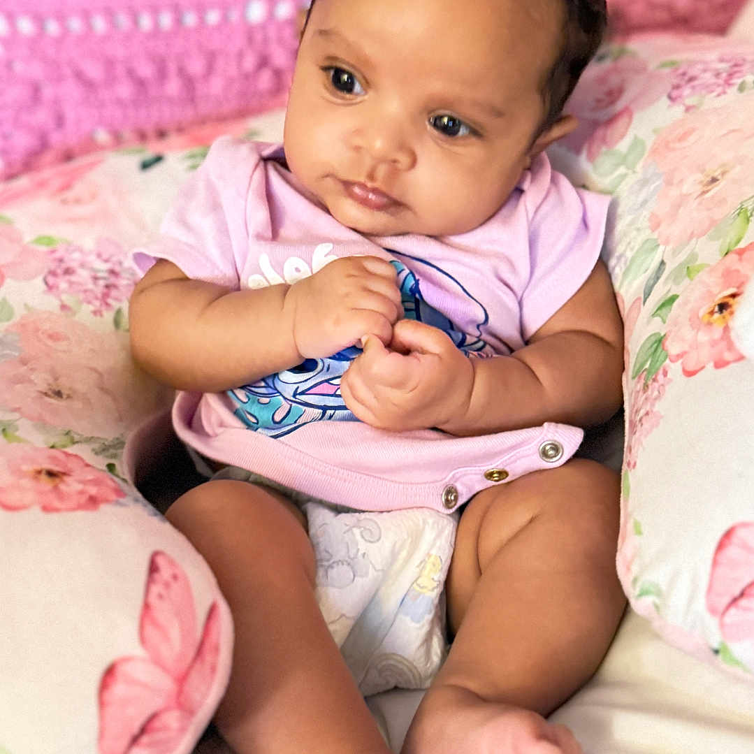 Alivia is registered to the contest to win money with this photo: baby, blanket, child, clothing, cozy, curly_hair, cute, diaper, feet, floral, hands, indoor, infant, person, pillow, pink, portrait, resting, soft_lighting, young