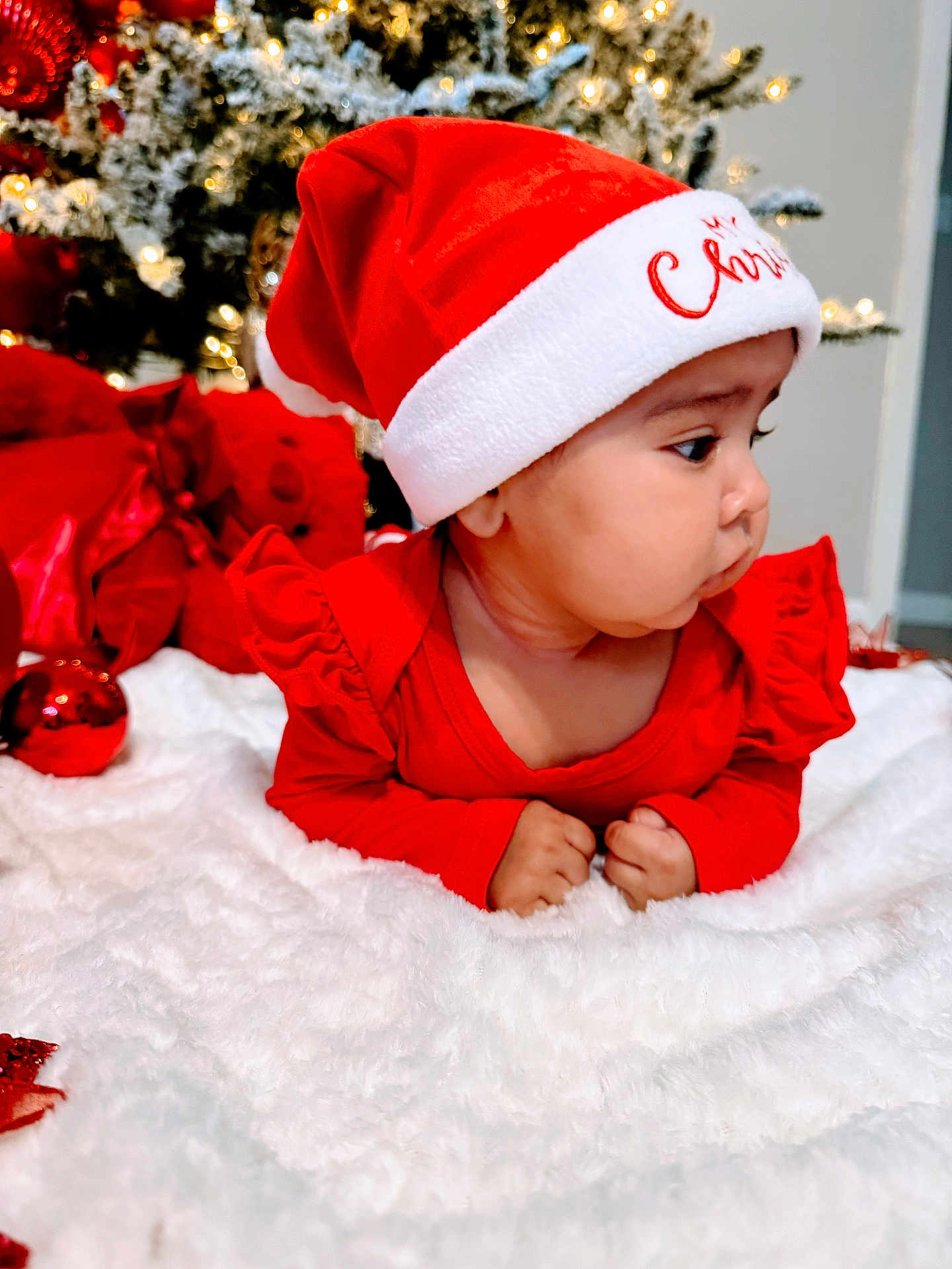 Naisha joined the competition — help win amazing prizes! baby, infant, christmas, santa_hat, red_clothing, blanket, holiday, decorations, christmas_tree, festive, cute, face, child, indoors, celebration, winter, smiling, holiday_lighting, soft_texture, toddler