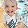 Alvin is registered to the contest to win money with this photo: child, toddler, smiling, happy, portrait, close_up, indoor, home, blond_hair, blue_eyes, teeth, white_shirt, nike_shirt, clothing, standing, play_mat, wood_floor, furniture, colorful_background, candid