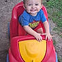 child, toddler, smiling, toy_car, outdoor, grass, concrete, red, yellow, blue, shorts, shirt, happy, person, play, summer, cute, kid, hands, face