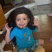 Alvin joined the competition — help win amazing prizes! child, toddler, smiling, sitting, chair, long_hair, dark_hair, blue_shirt, plaid_shorts, indoor, living_room, wooden_floor, rug, toys, window, furniture, portrait, happy, playful, photography
