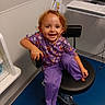 toddler, child, smiling, sitting, chair, purple_clothing, pajamas, red_hair, portrait, indoor, office, printer, computer, floor, cable, furniture, happy, young_child, casual, photograph
