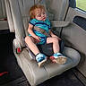 child, toddler, sleeping, nap, car, car_seat, seatbelt, vehicle, travel, road_trip, indoors, portrait, red_hair, striped_shirt, blue_shoes, sneakers, window, leather_seat, bottle, daylight