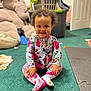 toddler, child, smiling, floral_onesie, curly_hair, green_carpet, plush_teddy_bear, laundry_basket, clothes, toys, indoor, playroom, sitting, happy, cute, person, footed_pajamas, baby, carpet, home