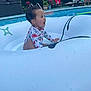 toddler, child, swimming_pool, inflatable_float, water, summer, outdoor, happy, sitting, swimsuit, excitement, water_droplets, recreation, leisure, people, adult, chair, fence, plant, daytime