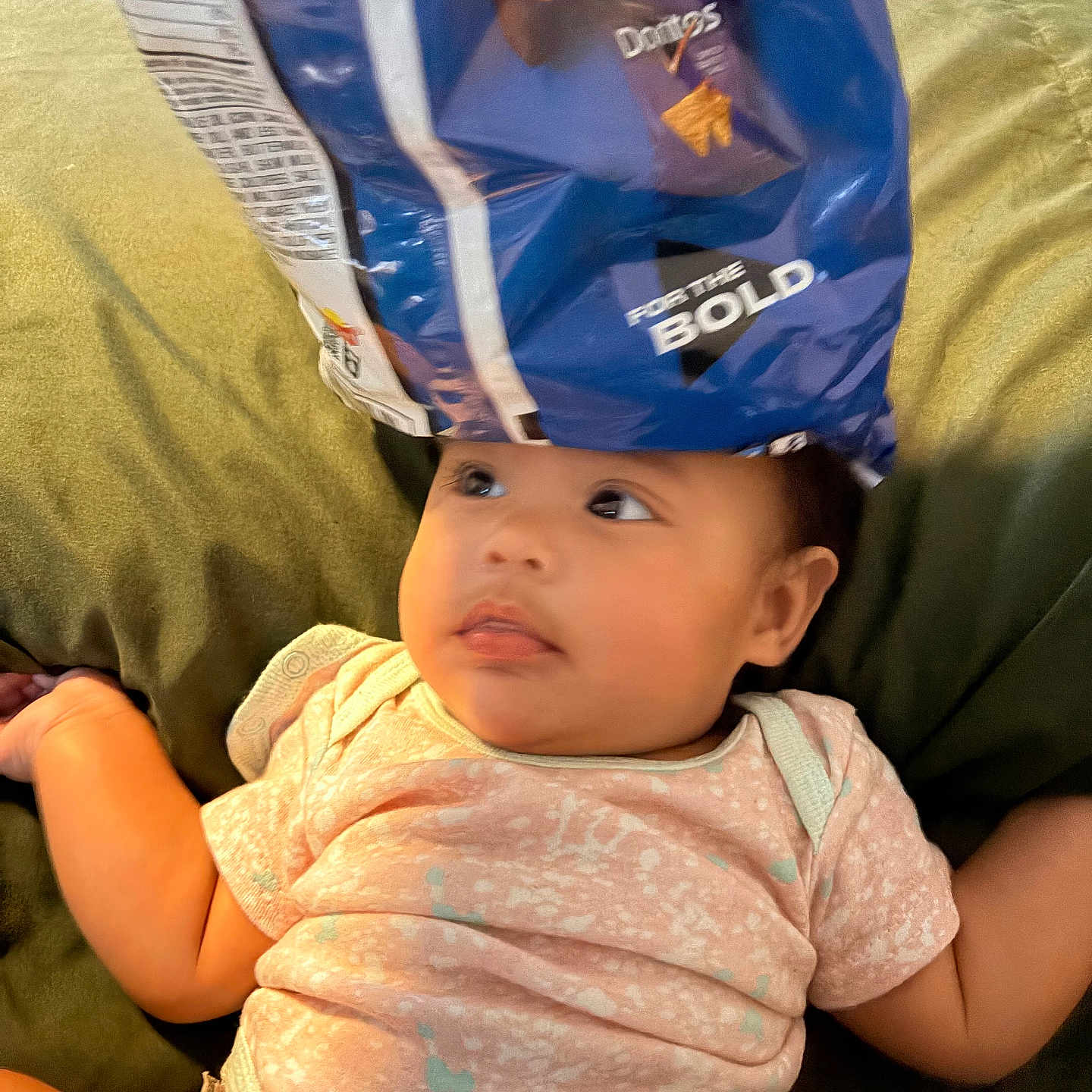 Priyah joined the competition — help win amazing prizes! baby, infant, child, face, portrait, sitting, lying_down, curious, cozy, cushion, green, clothing, pink_shirt, snack_bag, blue, funny_hat, indoor, home, close_up, humor