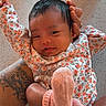 Priyah is registered to the contest to win money with this photo: baby, infant, floral_clothing, pink_socks, tattoo, arms, smile, face, person, indoor, holding, cute, newborn, skin, hand, table, expression, comfort, resting, cozy