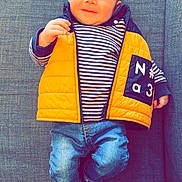 Tylio participe au concours pour gagner de l'argent avec cette photo : baby, child, infant, smiling, yellow_vest, striped_shirt, jeans, socks, couch, gray_fabric, indoor, portrait, cute, happy, person, young_child, seated, casual_clothing, relaxed, home