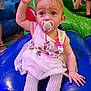 Alisha is registered to the contest to win money with this photo: baby, blue, child, colorful, cute, dress, fun, hand_raised, indoor, inflatable, pacifier, person, pink, play_area, playground, seated, tights, toddler, toy, young_child