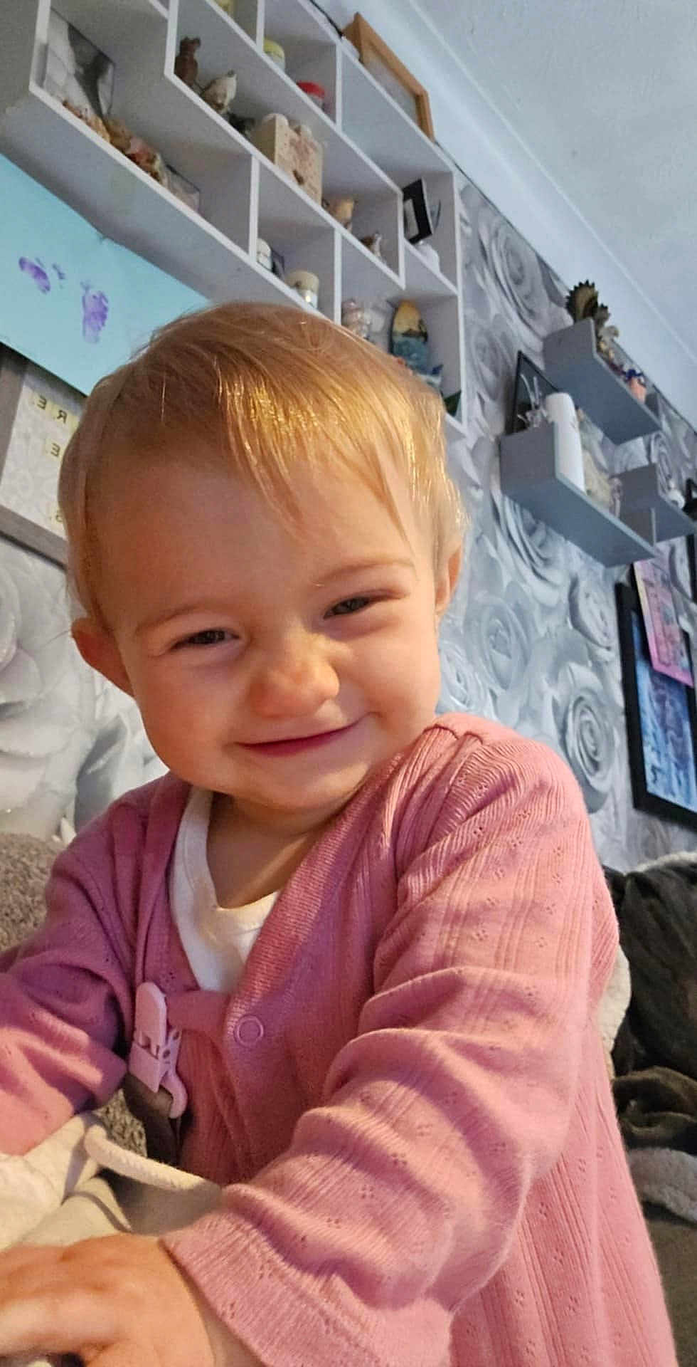 Alisha joined the competition — help win amazing prizes! toddler, child, smiling, pink_cardigan, indoor, living_room, wallpaper, shelves, decorations, face, happy, cute, playful, person, home, young_child, blond_hair, portrait, cozy, candid