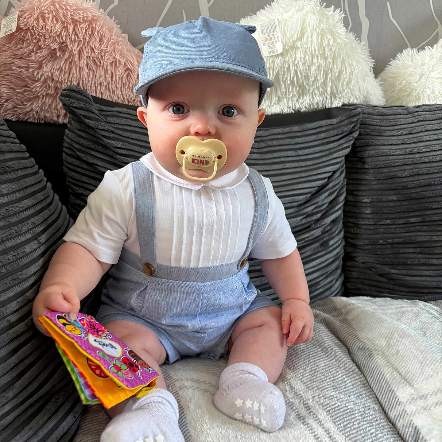 Hunter is registered to the contest to win money with this photo: baby, blanket, cap, child, clothing, couch, cute, fabric_book, face, home, indoor, infant, pacifier, person, pillows, seated, socks, soft, suspenders, toy