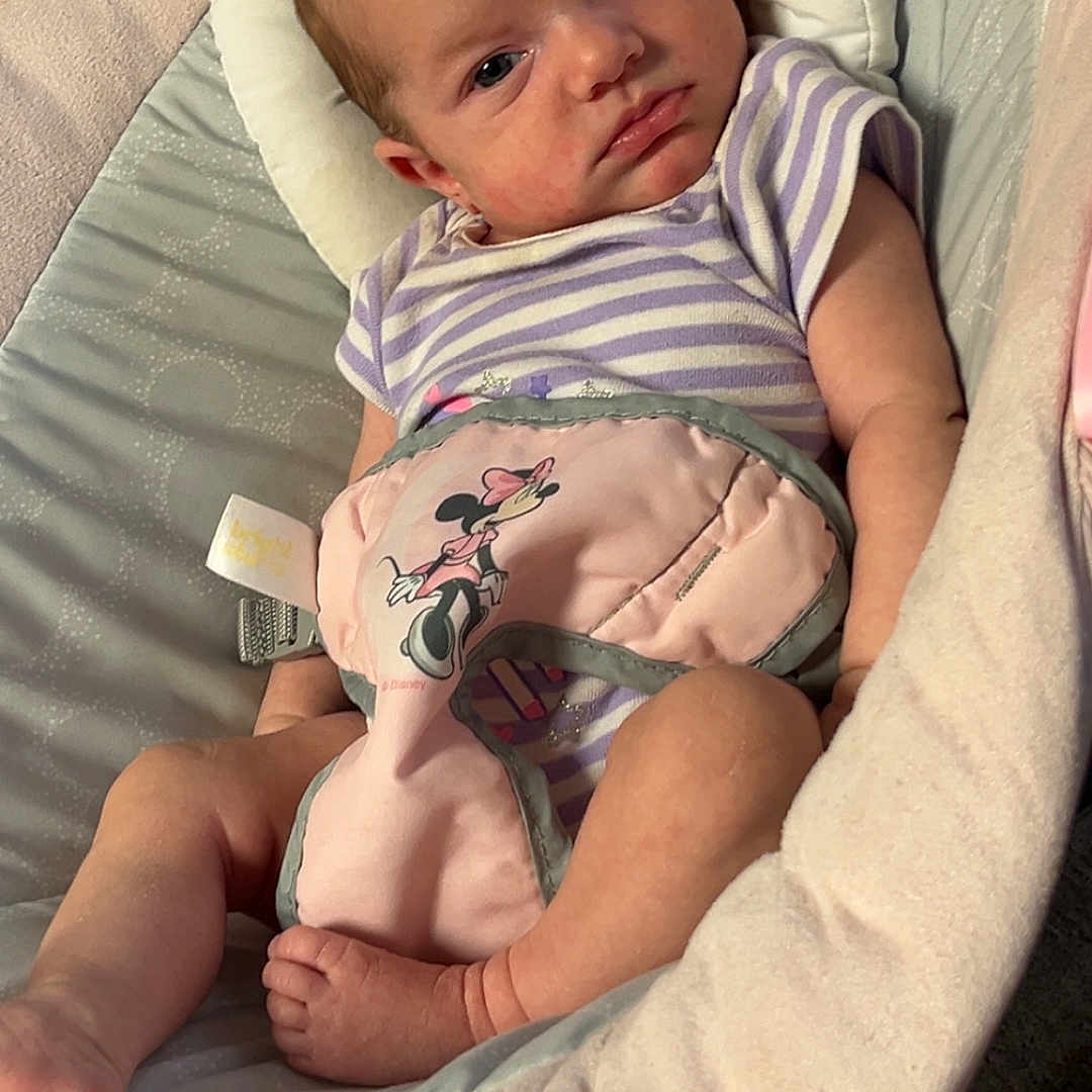 Wynter is registered to the contest to win money with this photo: baby, baby_seat, child, comfort, cushion, cute, face, feet, head_support, indoor, infant, minnie_mouse, newborn, onesie, person, plush, purple_stripes, relaxed, resting, soft_toy