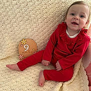 Nadia joined the competition — help win amazing prizes! baby, infant, 9_months, red_clothing, smile, face, sitting, blanket, crochet_blanket, wooden_sign, milestone, cute, child, indoors, happy, portrait, person, head, feet, hand