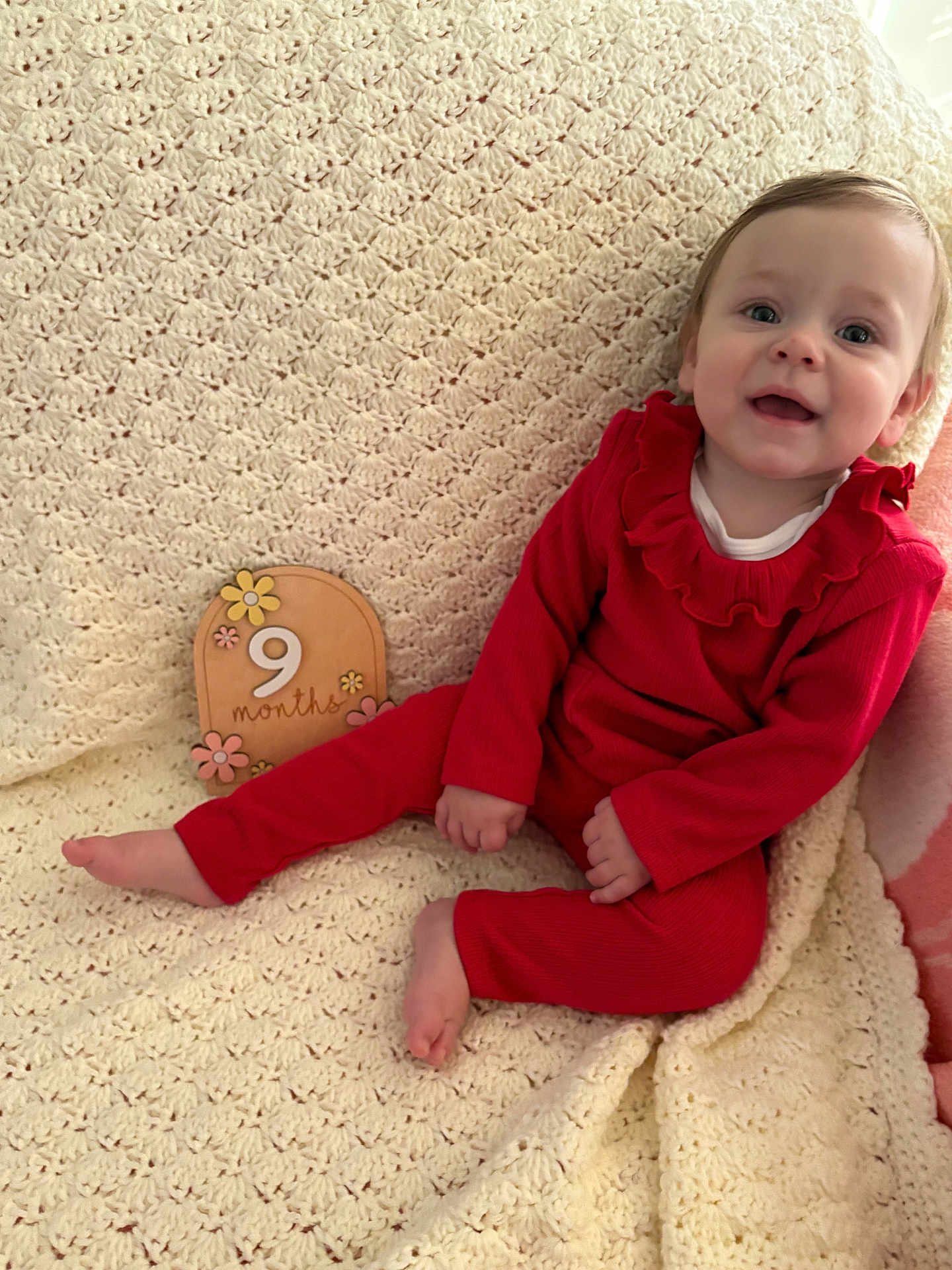 Nadia joined the competition — help win amazing prizes! baby, infant, 9_months, red_clothing, smile, face, sitting, blanket, crochet_blanket, wooden_sign, milestone, cute, child, indoors, happy, portrait, person, head, feet, hand