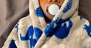 Kysin is registered to the contest to win money with this photo: baby, child, pacifier, robe, elephant_pattern, blue, white, blanket, soft_texture, hood, infant, lying_down, face, eyes, cozy, warm_clothing, indoors, portrait, cute, expression