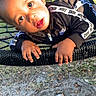 child, toddler, boy, outdoor, playground, swing, rope_swing, nike, clothing, black_jacket, face, hands, sunlight, grass, dirt, fence, car, residential, curious, expression