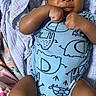 baby, infant, onesie, blue_clothing, animal_print, blanket, lying_down, fists, curious_expression, child, cute, indoors, portrait, skin, face, arms, legs, young_child, sleeping_area, soft_fabric
