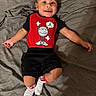 baby, child, smile, red_shirt, black_shorts, white_socks, cartoon_graphic, basketball, lying_down, blanket, indoors, cute, happy, portrait, infant, clothing, person, skin, head, feet