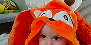 Alèzïo a rejoint le concours — aidez-le/la à gagner de superbes lots ! baby, child, orange_hoodie, fox_costume, plush_toy, stuffed_animal, toy, hand, indoor, smile, cute, face, person, childrens_clothing, soft_texture, seated, cozy, young_child, playful, bright_colors