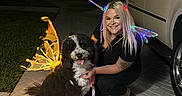 Coco joined the competition — help win amazing prizes! woman, dog, fairy_wings, night, driveway, pavement, car, smiling, pet, outdoor, costume, glowing, black_and_white_dog, kneeling, happy, suburban, animal, person, light, cute