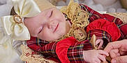 Sienna Mae is registered to the contest to win money with this photo: baby, sleeping, infant, bow, headband, lace, red_clothing, plaid, hand, finger, adult_hand, close_up, soft_lighting, cozy, cute, peaceful, portrait, indoors, child, smile